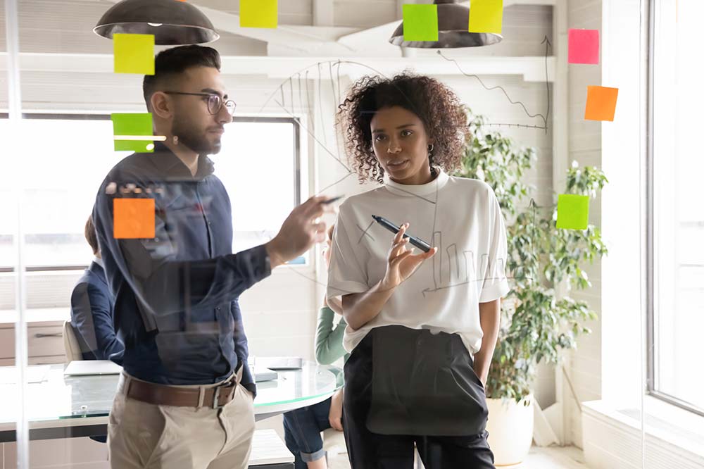 Two people drawing on a see through surface coming up with ideas